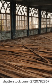 Interior of an abandoned historic palace complex featuring large windows, peeling paint and broken wooden planks on the floor. The space resembles a former ballroom, gallery or orangery, reflecting architectural decay, renovation or restoration concept. No people.