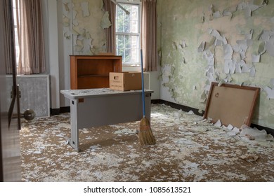 Interior Of Abandoned Office With Peeling Paint Desk And Bookshelves With Broom.