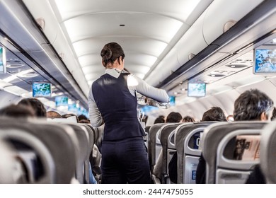 Interior of airplane with passengers on seats and stewardess in uniform walking the aisle, serving people. Commercial economy flight service concept