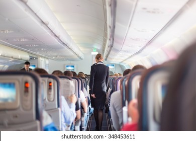 Interior del avión con pasajeros en asiento durante el vuelo. Guardias con uniforme azul oscuro caminando por el pasillo. Composición horizontal.