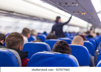 Interior of airplane with passengers on seats and stewardess walking the aisle.