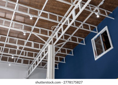 Interior architecture featuring sturdy and inviting industrial metal truss structure under wood roof deck with modern ceiling lighting against blue painted wall
