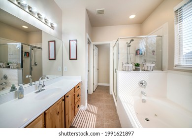 Interior Of A Bathroom With Craftsman's Style Vanity. There Is A Sink With White Top And Old Hollywood Lighting Fixture Across The Tub Against The Window Beside The Shower Stall With Glass Enclosure.