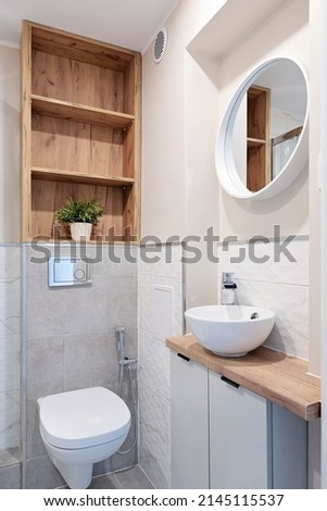 Interior of bathroom in design style with ceramic bathroom sink on wooden counter, round mirror on the wall and wc. Clean washroom in hotel. Vertical.