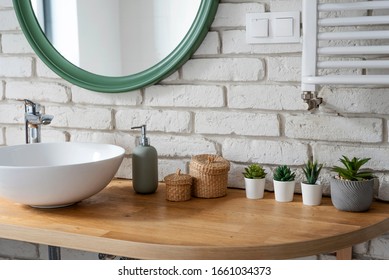 Interior of bathroom with modern design. White bricks,design basin and wooden counter with cactus. Bright indoor in industrial style and modern architecture.