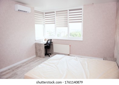 Interior Of Bedroom After Being Renovated. Room In Bright Colors With New Renovation. Large Bed, Air Conditioning And Computer Table Near Window. Windows With Roller Blinds On Background.