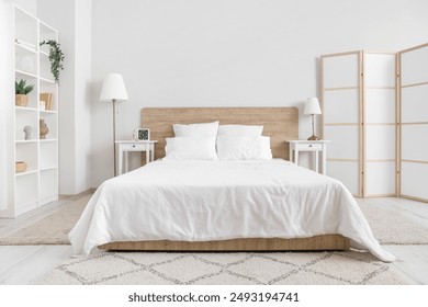 Interior of bedroom with bed, shelving unit and folding screen