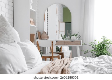 Interior of bedroom with dressing table, mirror and bed near white brick wall
