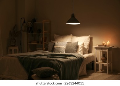 Interior of bedroom with green blankets on bed, burning candles and glowing lamp at night - Powered by Shutterstock