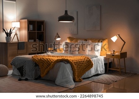 Interior of bedroom with knitted plaid on bed and glowing lamps at night