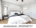 Interior bedroom with white lines duvet quilt black and blue accent pillows and throw blanket side tables of dark wood with small round white lamps ceiling fan large window mirror and soft curtains