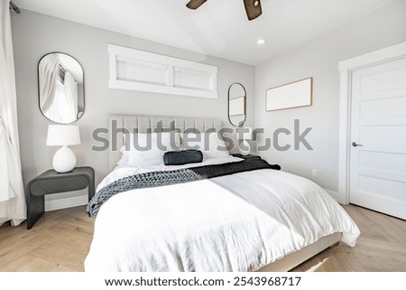Interior bedroom with white lines duvet quilt black and blue accent pillows and throw blanket side tables of dark wood with small round white lamps ceiling fan large window mirror and soft curtains
