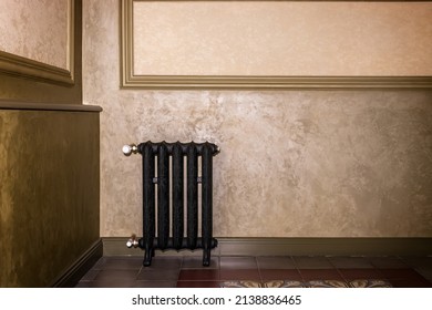 Interior with a black cast-iron radiator in the corner of the room against a beige wall.
