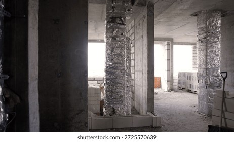 Interior of a building under construction, featuring raw concrete elements and foil insulation on ventilation shafts