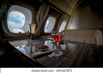 Interior Of A Business Class Of A Commercial Passenger Plane, An Armchair And A Window, A Table And A Cocktail Glass With A Drink And Almonds. Focus On A Glass.