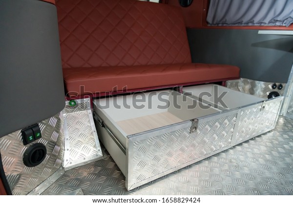The interior of\
the car in the back of a van converted into a motor home for\
off-road and travel with a brown leather interior, a folding table\
and aluminum floor trim.