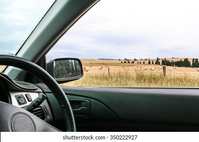 Interior Of Car With Steering Wheel And Country Side Of Paddocks With Hay Bails Visible Out Of Window And Trees In Rear Vision Mirror. Drive In The Country.