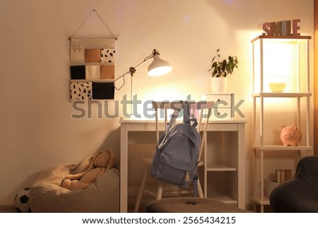 Interior of children's room with study table, shelf unit and glowing lamps at night