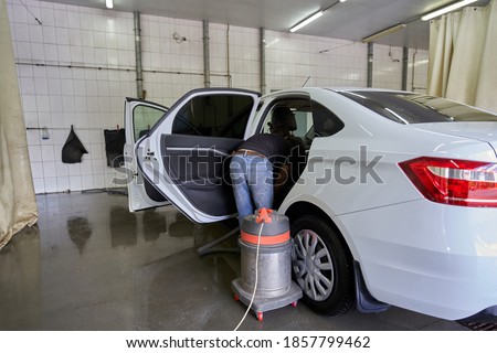 Interior cleaning with an industrial vacuum cleaner of a modern car in a car wash hangar.