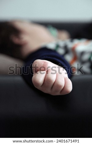 Interior close up photo view of a detail arm hand of a young baby kid child children male eurasian asian boy sleeping asleep napping resting rest on a couch sofa he is tired during his afternoon nap
