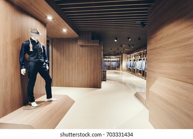 Interior Of A Clothing Store And Business Suits. Wall Covering Under A Tree. In The Foreground There Is A Maniken In A Suit And Hat.