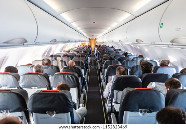 Interior of commercial airplane with\
unrecognizable passengers on their seats during flight shot from\
the rear of airplane.