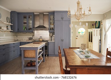 Interior Of A Country Style Kitchen With An Island, Dining Table And Modern Appliances In A Residental Home