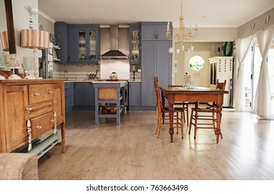 Interior Of A Country Style Kitchen In A Residental Home With An Island, Dining Table And Modern Appliances