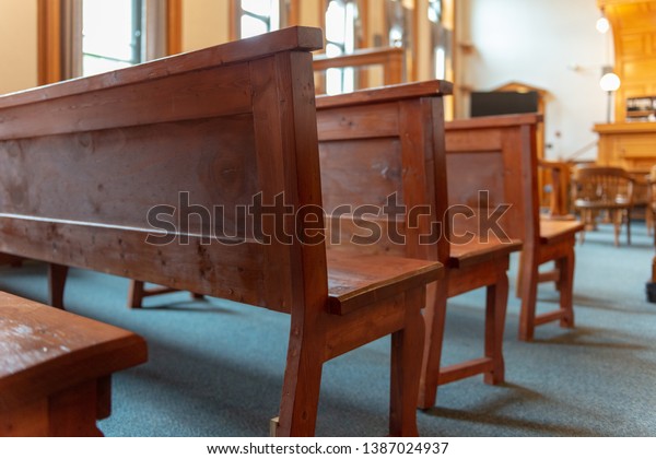 Interior of a courtroom with rows of witness or\
jury benches made of dark wood. The attorney chairs are in the\
front with the judge\'s bench.  The empty room is divided for\
witnesses and counsel\
lawyer