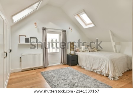 The interior of a cozy bedroom with slanted windows on the ceiling and a carpet on the floor