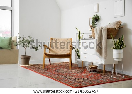 Interior of cozy living room with armchair, chest of drawers and vintage carpet