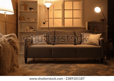 Interior of dark living room with sofa and glowing lamps in evening