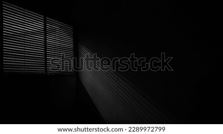 interior of dark room. shadow of the rays falling on the wall through the louvers. Light from the lamp and shadow on room wall from roller window shutter. night club. black and white.