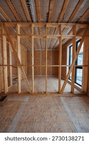 Interior daytime view shows stud framing, OSB, diagonal bracing, Pro clima membrane ceiling bays, tall black framed windows, conduits, and wood fibre loose fill prep.