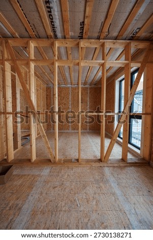 Interior daytime view shows stud framing, OSB, diagonal bracing, Pro clima membrane ceiling bays, tall black framed windows, conduits, and wood fibre loose fill prep.