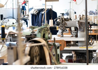 Interior of a deserted tailors shop with multiple work benches, equipment and a rack of completed handmade jackets in the background