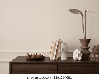 Interior design of aesthetic living room interior with copy space, wooden sideboard, vase with dried flowers, books, modern sculpture, beige wall with stucco and accessories. Home decor. Template.