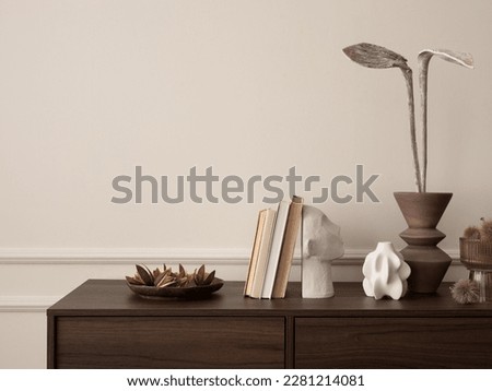 Interior design of aesthetic living room interior with copy space, wooden sideboard, vase with dried flowers, books, modern sculpture, beige wall with stucco and accessories. Home decor. Template.