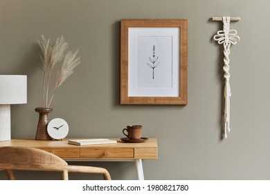 Interior design of boho living room with mock up poster frame. wooden desk, dried flowers in vase, rattan decoration, macrame, cup of coffee and clock in home decor. Boho home office. Template.