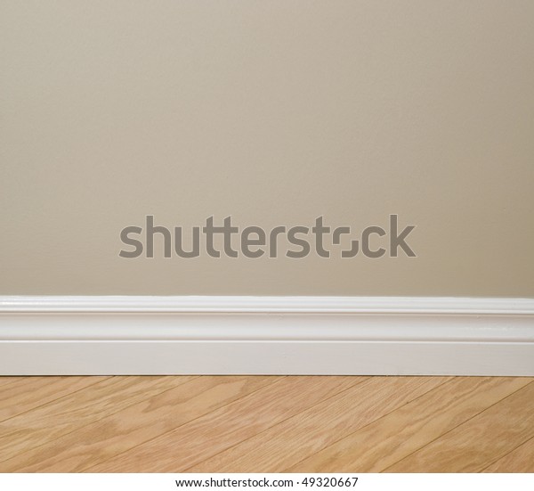 Interior design detail. Beige wall, clean white\
baseboard molding and wooden\
floor.