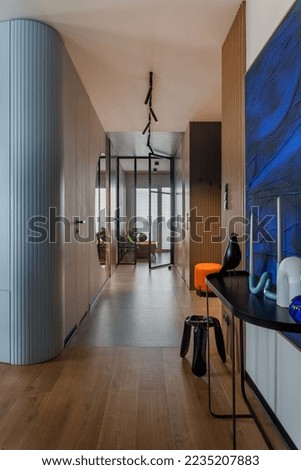 Interior design of harmonized hall with big blue painting, minimalistic blac consola, sculptures, candle in candlestick, wooden floor, modern stool and personal accessories. Home decor. Template. 