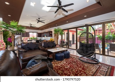 Interior design of house, home, villa feature leather couch, black sofa cushion, artificial flower on the table, carpet, ceiling fan, egg shape chair swing and a view of swimming pool from living room