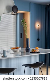 Interior design of kitchen interior with marble kitchen island, blue wall, black chokers, bowl with fruits, big window, cup, wooden floor, lamp on wall and personal accessories. Home decor. Template. - Shutterstock ID 2235207913