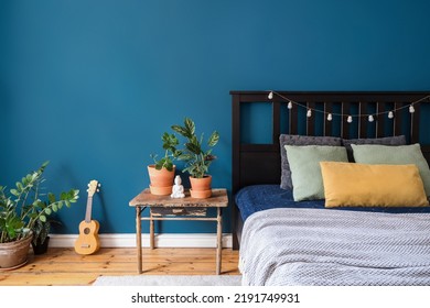 interior design of lounge room in bohemian style with comfort wooden bed with blanket and pillows, vintage table with decor, buddha figurine and green plant in pots and ukulele on floor