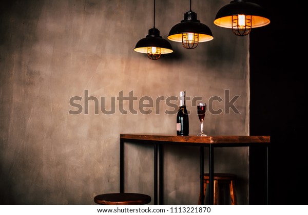 Interior design of restaurant or cafe.\
Side Photo of wooden table with bottle champagne or wine and glass\
with drink on it, three modern lamps above\
table