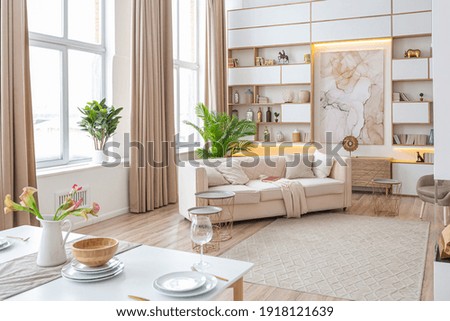 interior design spacious bright studio apartment in Scandinavian style and warm pastel white and beige colors. trendy furniture in the living area and modern details in the kitchen area.
