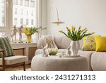 Interior design of spring living room with design sofa, furniture, vase with tulips, easter decorations, pillows and personal accessories. Home decor. Template. Easter holidays.