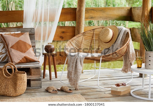 Interior design of  summer\
gazebo by the lake with stylish rattan armchair, coffee table,\
sofa, pillows, plaid and elegant accessories in modern decor.\
Summer vibes.