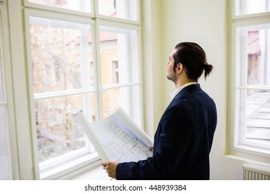 Interior designer with blueprint looking though window at creative office - Shutterstock ID 448939384