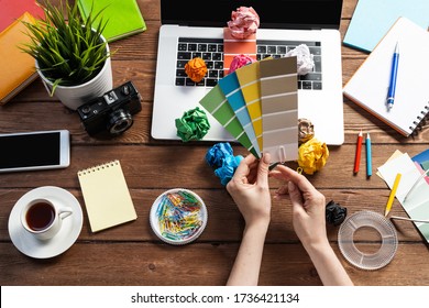 Interior Designer Choosing Colors From Swatches At Wooden Desk. Office Workplace With Laptop And Stationery. Selection Of Color Palette For Design. Professional House Renovation And Interior Redesign.